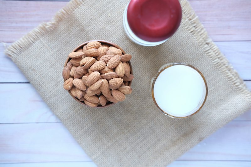 Bowl of almonds next to a glass of almond milk, with iced coffee in the background on a linen cloth
