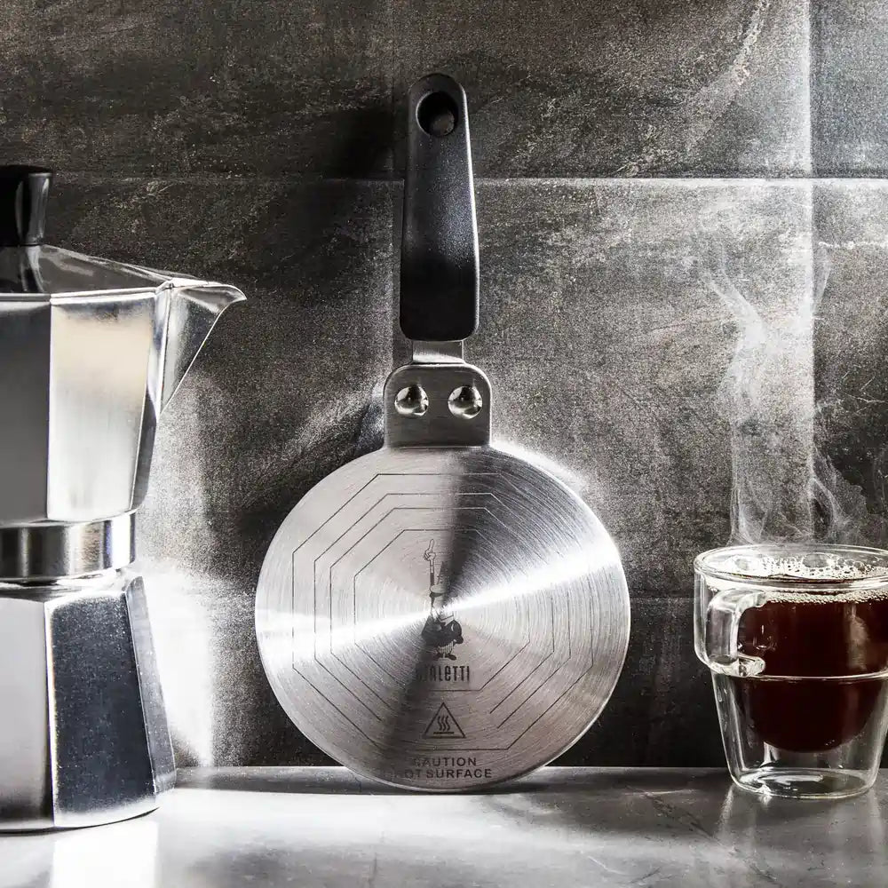 Adapter indukcyjny Bialetti 13 cm ze stali nierdzewnej obok kawiarki Moka i filiżanki kawy, płyta grzewcza do płyt indukcyjnych, zdjęcie lifestyle