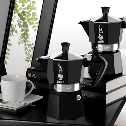 Czarna kawiarka Bialetti Moka Express 6 tz ustawiona na książkach w eleganckim wnętrzu – klasyczny design w matowej czerni z kontrastującym srebrnym wykończeniem.