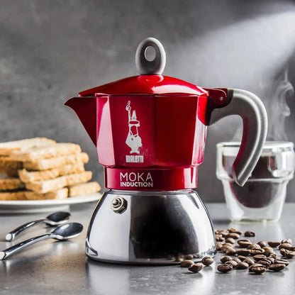 Czerwona kawiarka Bialetti Moka Induction podczas parzenia espresso, ziarna kawy i akcesoria w tle