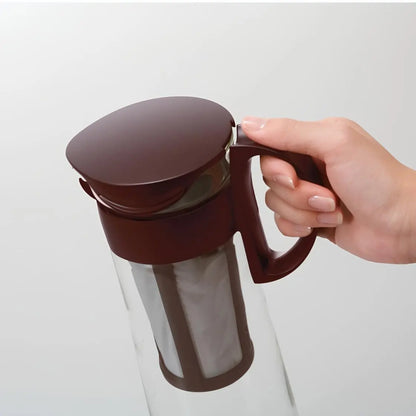 Dzbanek Hario Mizudashi do cold brew widziany z góry, trzymany w dłoni – wyraźny widok pokrywki, uchwytu i filtra w kolorze ciemnobrązowym.