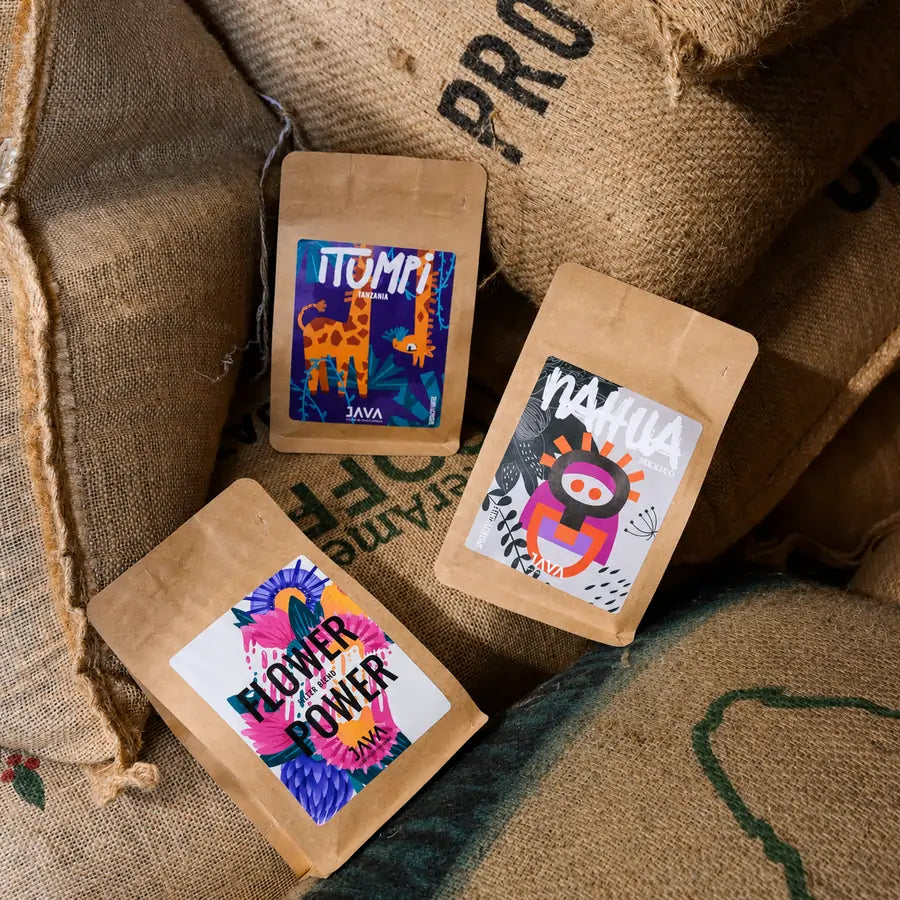 Trzy kawy specialty JAVA Coffee Roasters – Flower Power, Nahua Mexico i Tanzania Itumpi na workach jutowych z zieloną kawą w palarni .