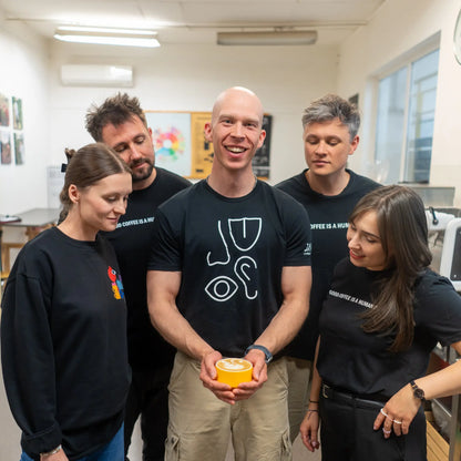 Zespół baristów JAVA Coffee Roasters z filiżanką kawy z latte art – uśmiechnięci, skupieni na jakości i wspólnej pasji do kawy rzemieślniczej.