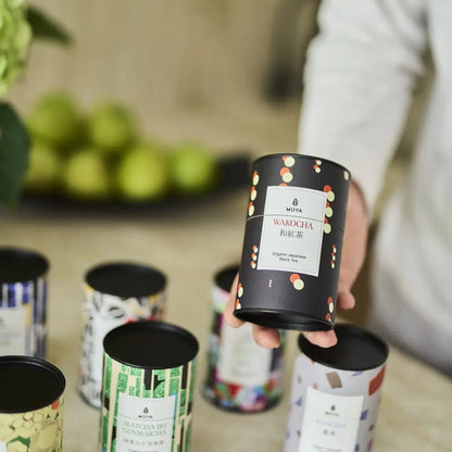 MOYA Wakocha – organiczna japońska czarna herbata trzymana w ręku, w otoczeniu innych herbat liściastych z kolekcji MOYA
