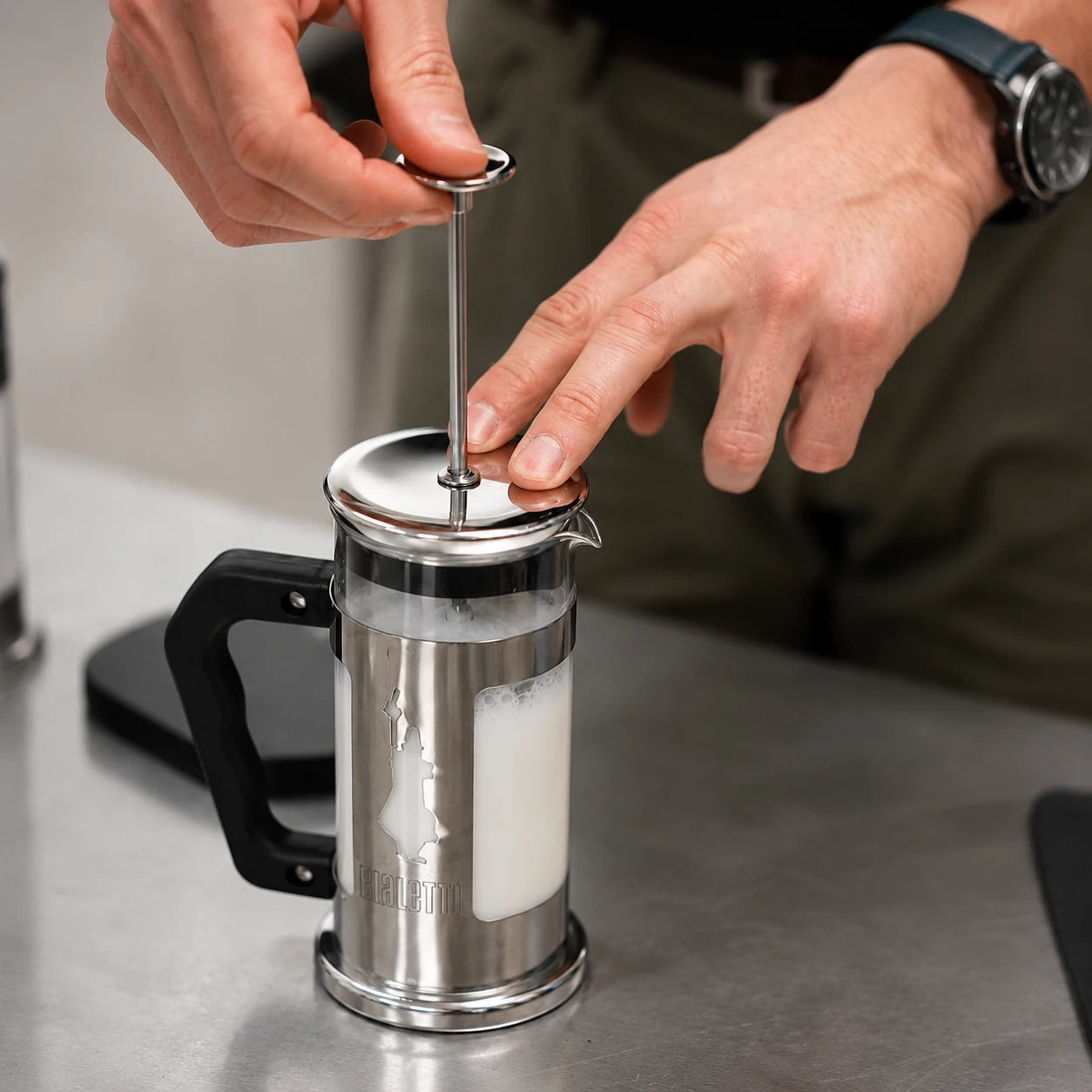Instruktor spienia mleko w ręcznym spieniaczu Bialetti podczas szkolenia baristycznego. Nauka przygotowania mikropianki do cappuccino i latte art.