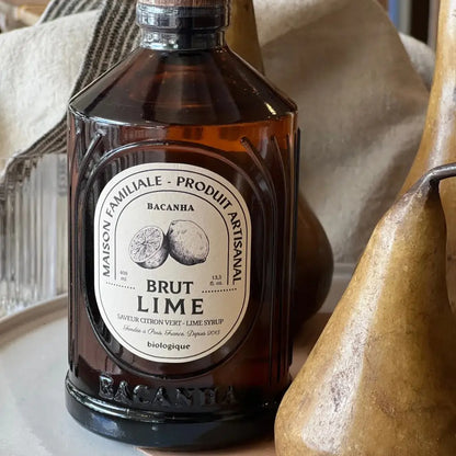Syrop Bacanha o smaku limonki – organiczny syrop w bursztynowej butelce, ustawiony w stylowej aranżacji z gruszkami i tekstyliami