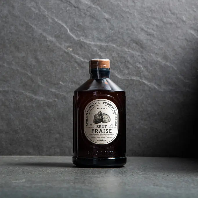 Syrop Bacanha o smaku truskawkowym – organiczny syrop w bursztynowej butelce na kamiennym tle