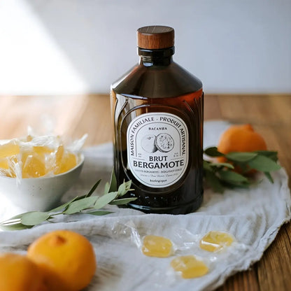 Butelka syropu Bacanha o smaku bergamotki na lnianej ściereczce, w otoczeniu cytrusów i cukierków – naturalny, organiczny syrop 400 ml