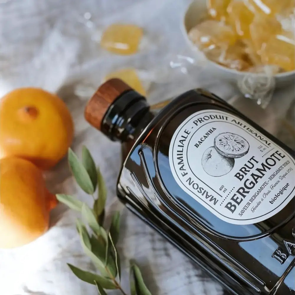 Leżąca butelka syropu Bacanha o smaku bergamotki w stylowej scenerii z cytrusami i liśćmi – naturalny, organiczny syrop do napojów i koktajli.