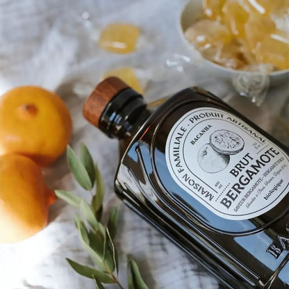 Leżąca butelka syropu Bacanha o smaku bergamotki w stylowej scenerii z cytrusami i liśćmi – naturalny, organiczny syrop do napojów i koktajli.