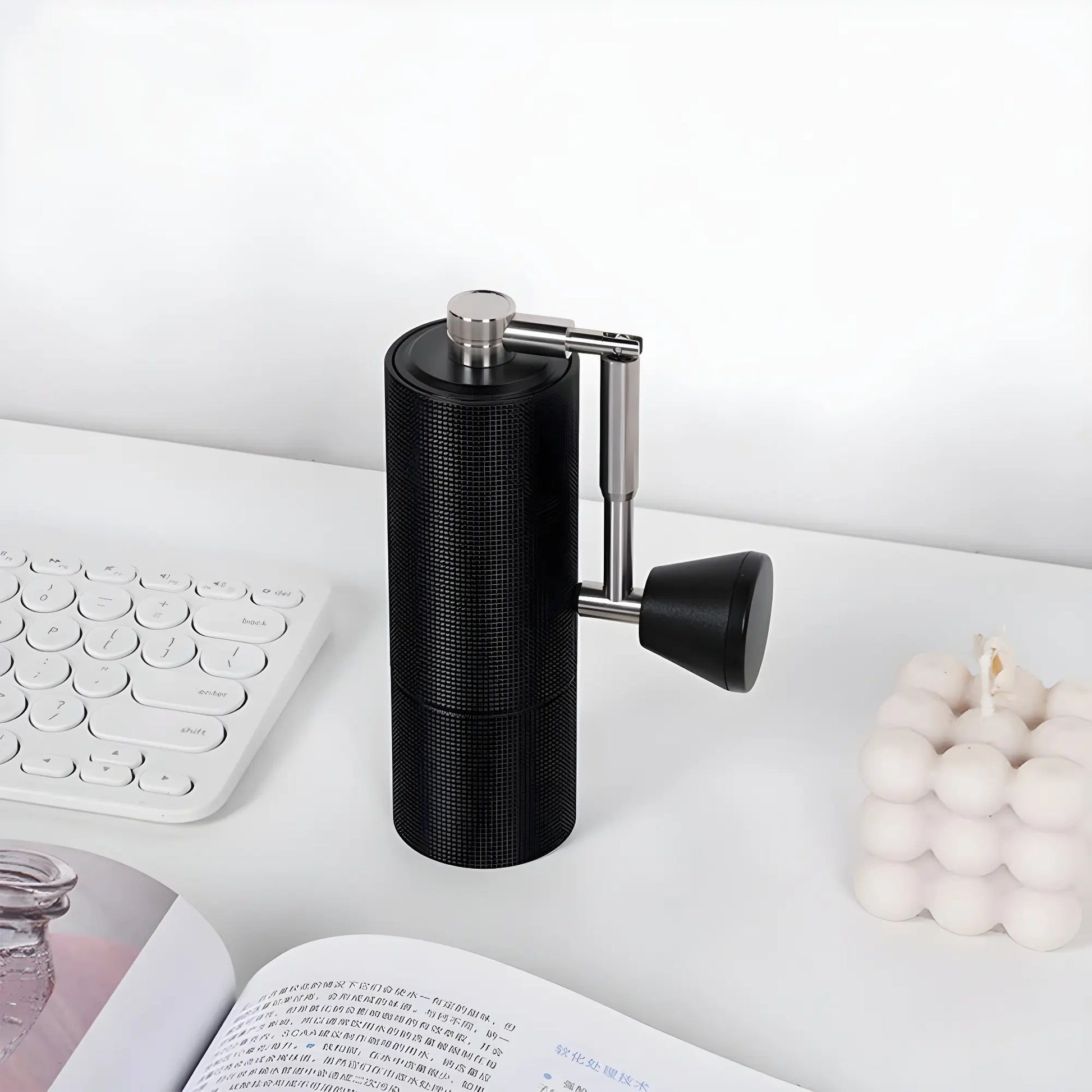 Ręczny młynek do kawy Timemore Chestnut C3s Pro Black ustawiony na biurku obok klawiatury, świeczki i otwartej książki – elegancki i minimalistyczny design