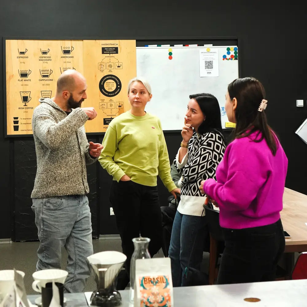 Uczestnicy warsztatów kawowych rozmawiają podczas szkolenia w palarni JAVA Coffee Roasters, na stole akcesoria do parzenia kawy i paczka kawy