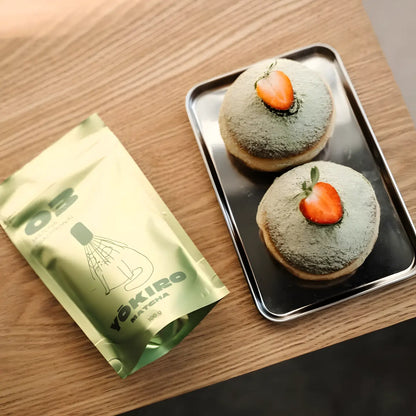 Lifestyle flat lay z matchą Yōkiro Traditional – opakowanie matchy obok pączków z matchą i truskawką na drewnianym stole